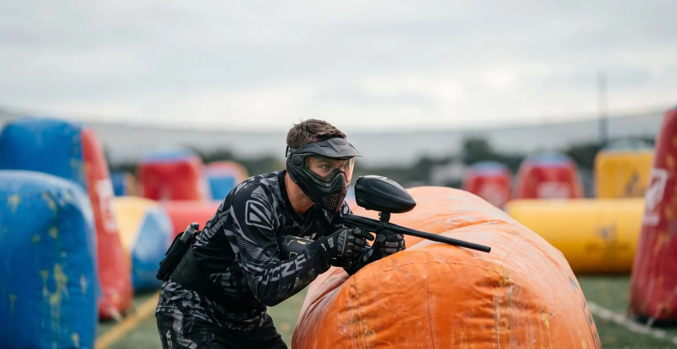 Joueur de paintball sportif équipé d'un masque et d'un marqueur, concentré avant le départ d'un point sur un terrain de compétition symétrique