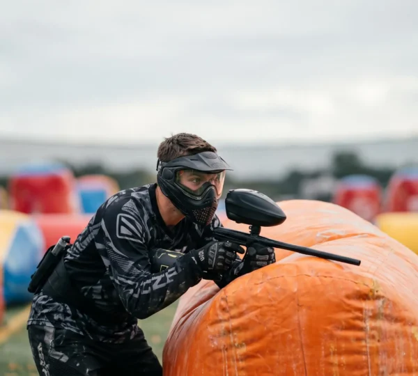Joueur de paintball sportif équipé d'un masque et d'un marqueur, concentré avant le départ d'un point sur un terrain de compétition symétrique