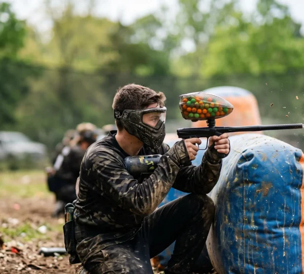 Joueur de paintball en action dont le loader alimente le marqueur en billes de peinture sans interruption sur un terrain extérieur
